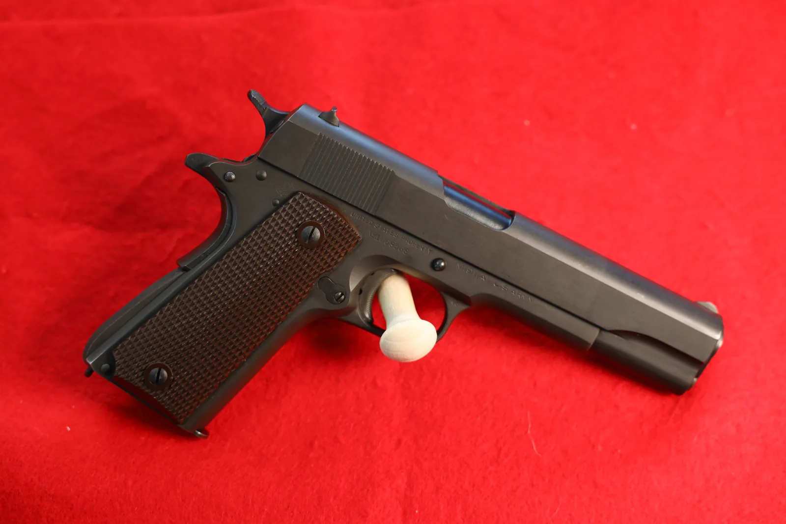 Military-pattern 1911 pistol with checkered grips on red felt